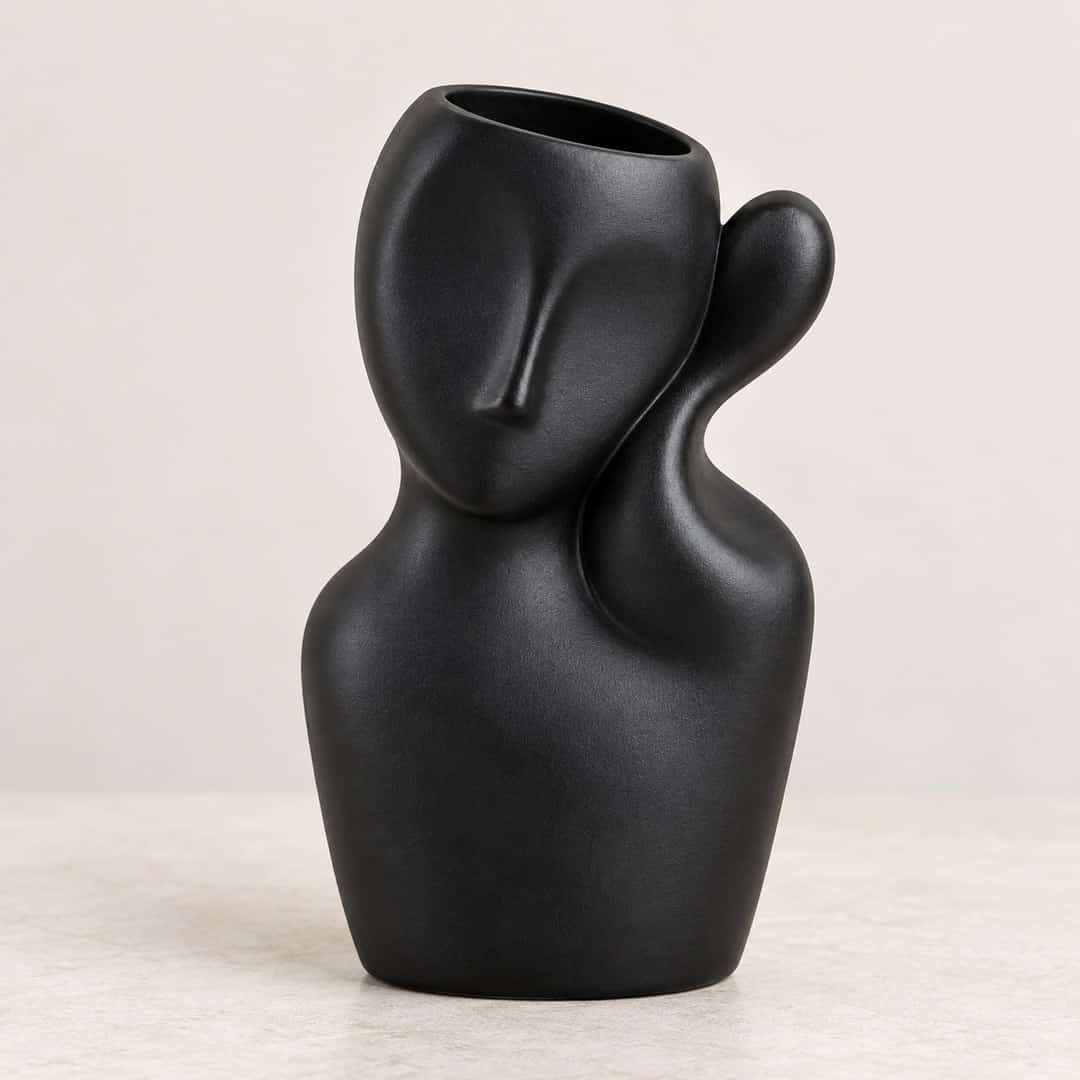 matte black abstract face vase with curved handles on a light tabletop
