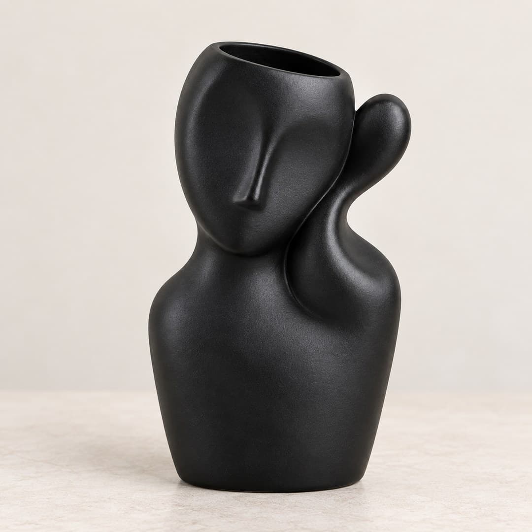 matte black abstract face vase with curved handles on a light tabletop